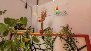 Een receptiebalie met een bord waarop 'First Hostel' staat, omringd door diverse planten en moderne hanglampen.
