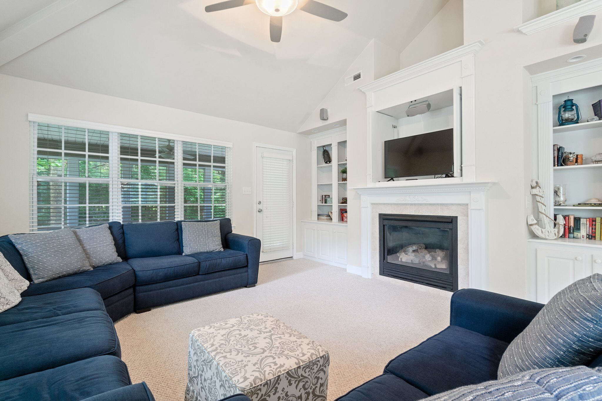 A living room with a sectional sofa, a fireplace, and a television mounted above it.