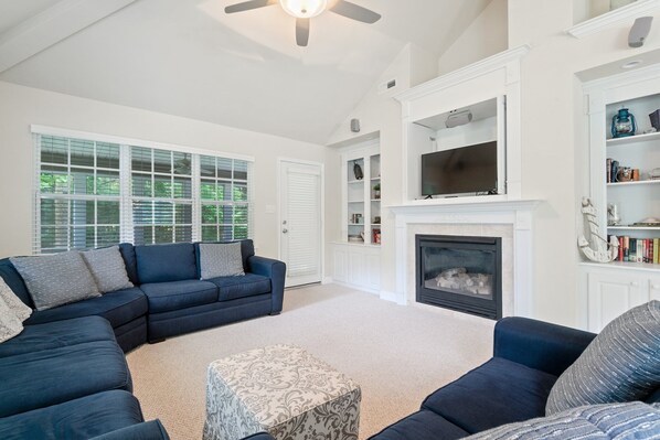 A living room with a sectional sofa, a fireplace, and a television mounted above it.