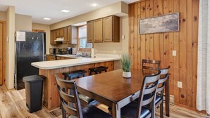A kitchen with wooden cabinets, a refrigerator, a dining table with chairs, and a potted plant. - “Bearly-Be-Haven” w/hot tub, firepit, Bearly-Be-Haven (Basye)