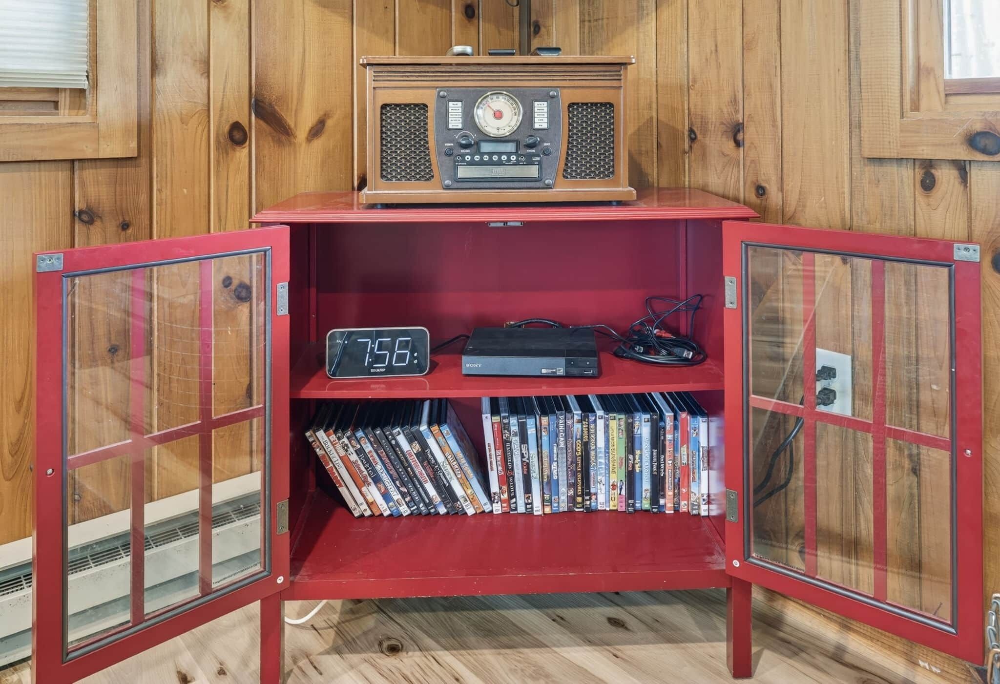 Un meuble de rangement rouge pour appareils multimédias, avec une radio ancienne, une horloge Sony et une collection de DVD.