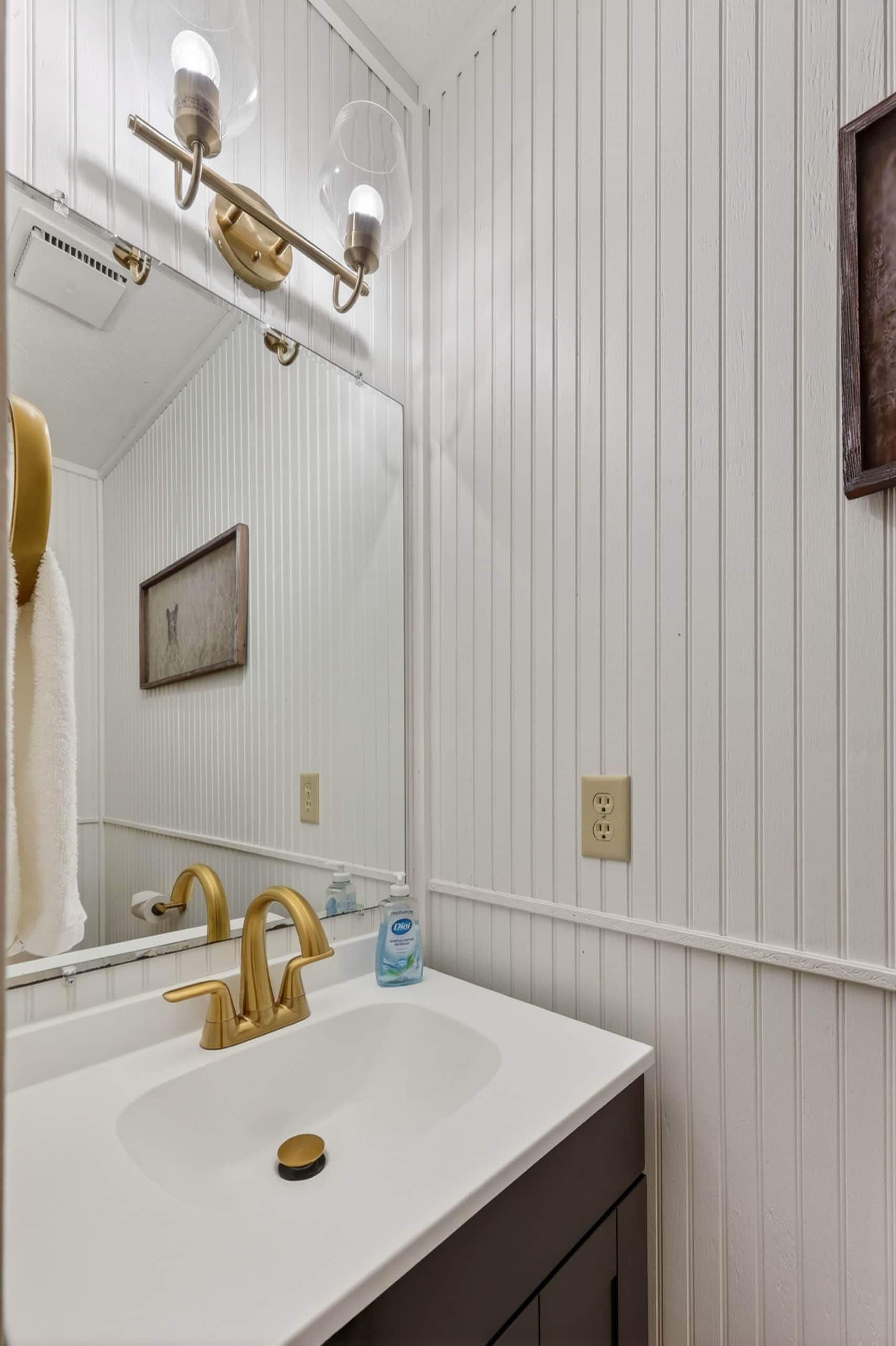 Un baño con lavamanos blanco, grifo dorado y espejo con luces.