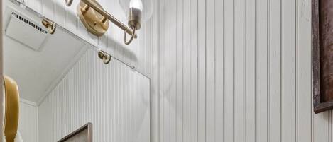 Un baño con lavamanos blanco, grifo dorado y espejo con luces.