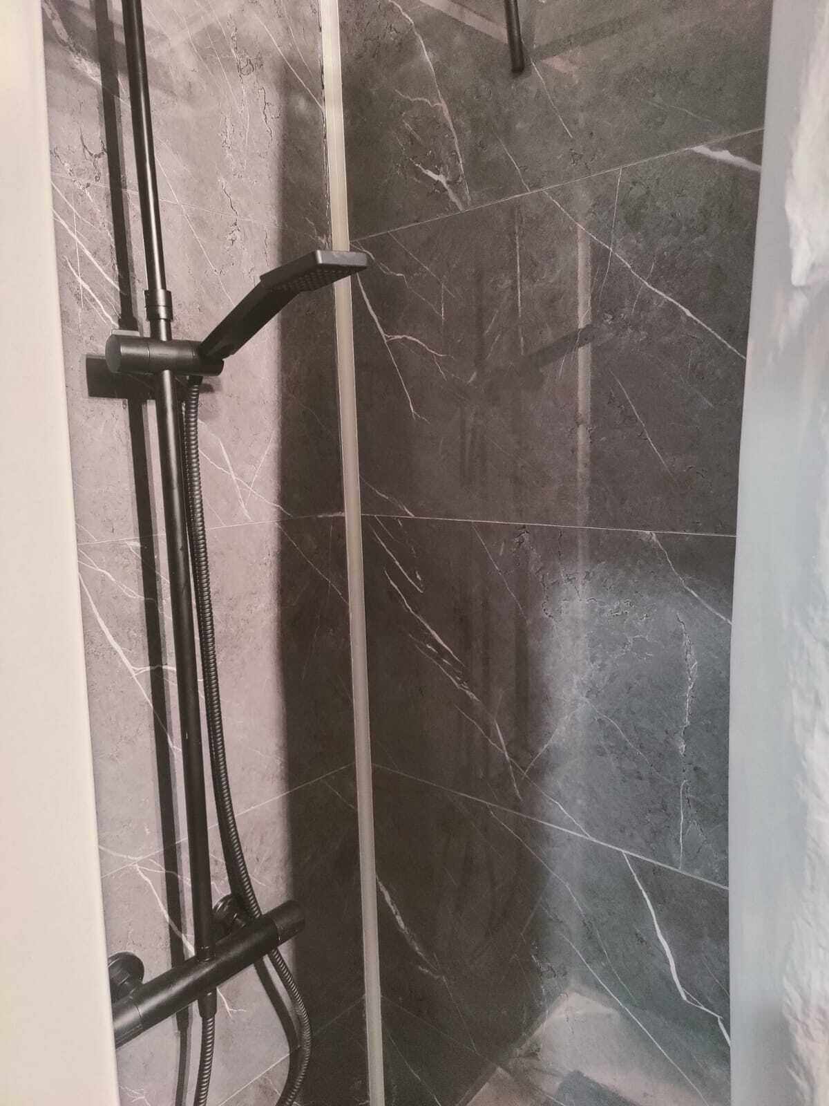 Douchegedeelte met een marmeren wand en een metalen douchekop.