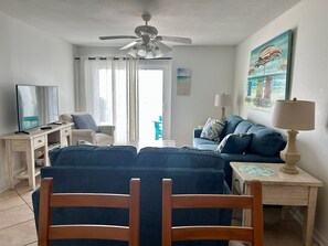 Ein Hotelzimmer mit Bett, Schreibtisch, Stuhl, Fernseher, Deckenventilator, einem Gemälde und einem Fenster mit Vorhängen.