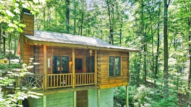 A wooden cabin with a balcony, surrounded by a forest.