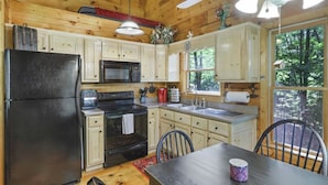 A cabin kitchen with wooden walls, a black refrigerator, a microwave, a stove, and a sink.
