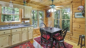 A wooden cabin interior with a kitchen, dining area, and large windows.