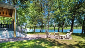 A covered deck with a staircase leading to a platform, surrounded by a grassy area with chairs and a table. - Perfect Waterfront Getaway between the Lakes  (Montello)