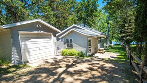 Two small, single-story cabins with attached garages, surrounded by trees and a gravel driveway. - Perfect Waterfront Getaway between the Lakes  (Montello)