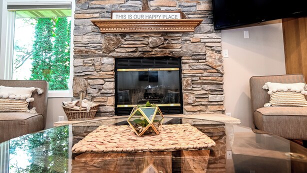 A cozy living room with a stone fireplace, two comfortable sofas, a glass coffee table, and a sign above the fireplace that reads "THIS IS OUR HAPPY PLACE". - Perfect Waterfront Getaway between the Lakes  (Montello)
