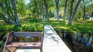 A wooden bench on a bridge over a calm water body, surrounded by lush greenery and trees. - Perfect Waterfront Getaway between the Lakes  (Montello)