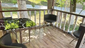 Une terrasse en bois avec deux chaises noires et une petite table, entourée de rampes blanches et d’arbres.