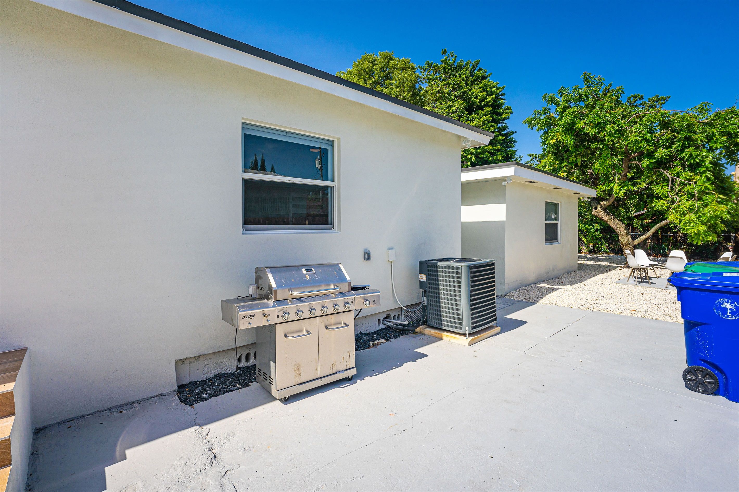 Esterno di una residenza con un edificio bianco, un barbecue e un cestino blu.