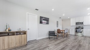 Een moderne keuken met witte kasten, een magnetron en een inbouwoven. Er is een eethoek met een tafel en stoelen.