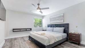 Een slaapkamer met een bed, nachtkastje, plafondventilator, raam en een wandplank.