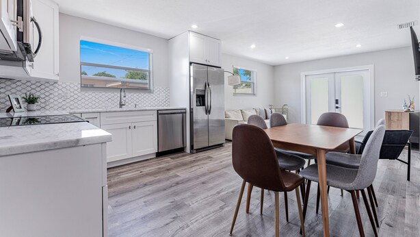 Een moderne keuken met witte kasten, een roestvrijstalen koelkast en een eethoek met een houten tafel en stoelen.