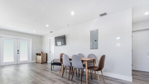 Een moderne eetruimte met een houten tafel en grijze stoelen, een aan de muur bevestigde televisie en een houten kast.