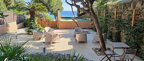 Un espace extérieur aménagé avec des chaises et une table, entouré de verdure et d’un mur en pierre.
