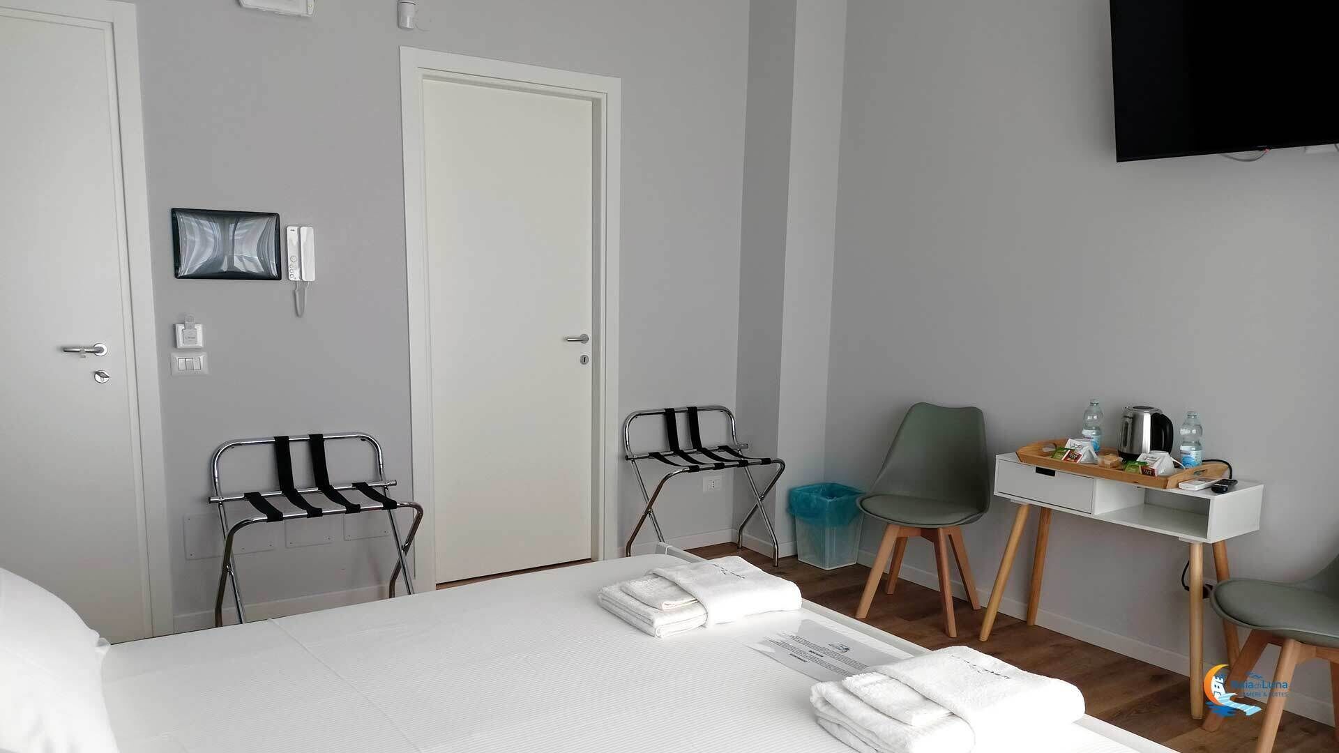 A hotel room with a bed, two chairs, a small table with items, and a TV on the wall.