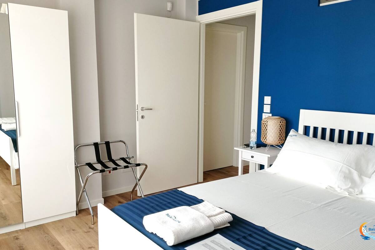 Ein Hotelzimmer mit einem Bett, einem Sessel, einem Nachttisch und einer Tür zu einem anderen Raum.