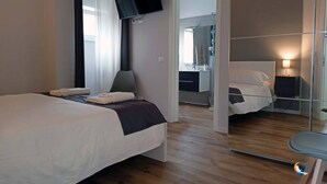 Ett modernt hotellrum med en stor säng, en spegel, ett skrivbord och ett badrum som syns genom en glasvägg.