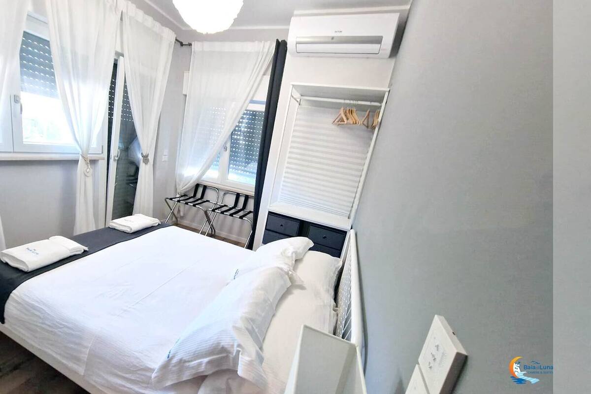 Ein Hotelzimmer mit Bett, einem Fenster mit Vorhängen, einer Klimaanlage und einem kleinen Tisch mit einem Handtuch.