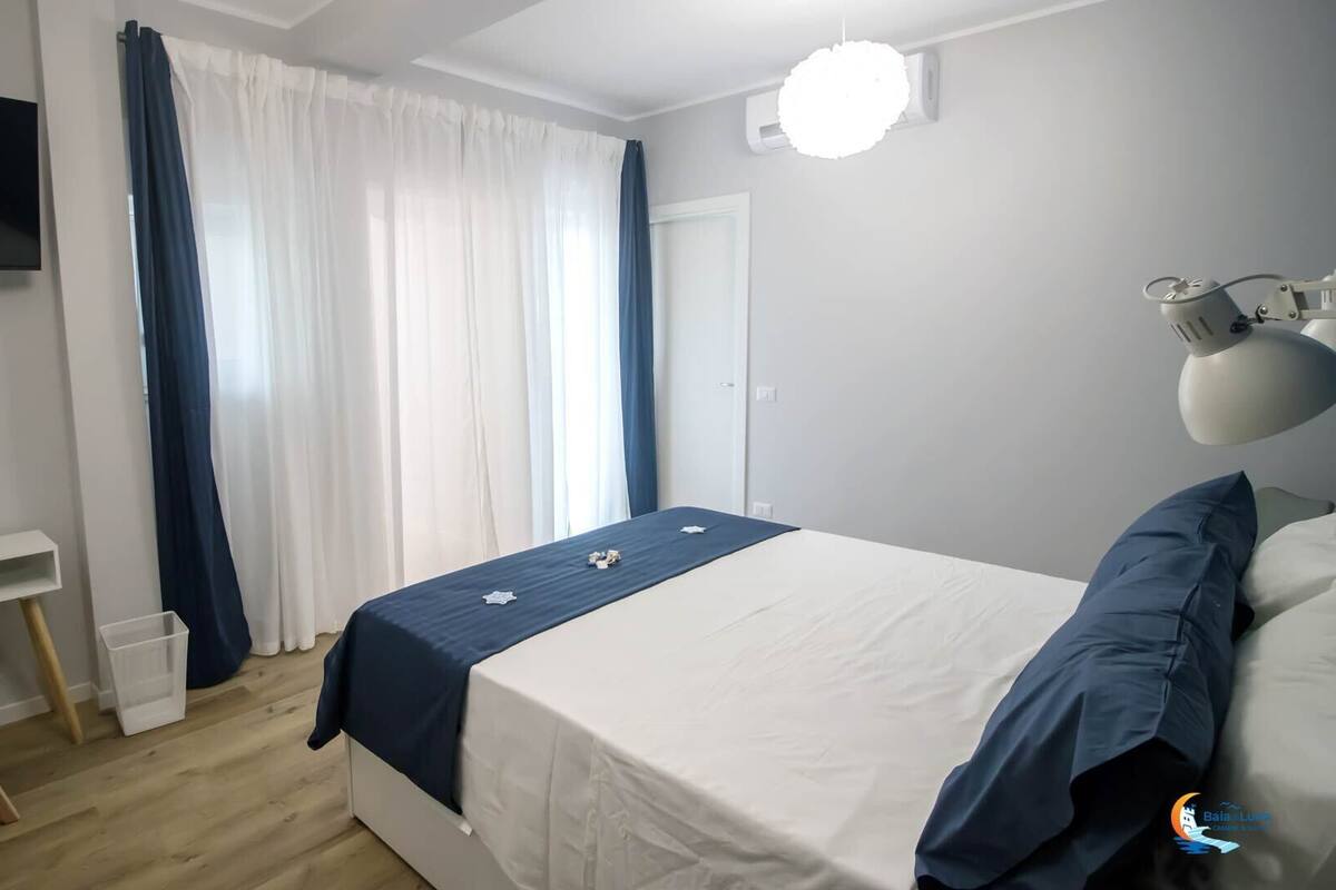 Ein Schlafzimmer mit Bett, Schreibtisch, Stuhl, Fernseher und einem Fenster mit Vorhängen.