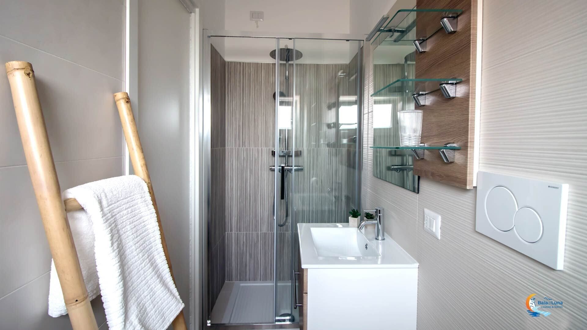 A modern bathroom with a glass shower enclosure, a white sink, and a mirror with glass shelves.
