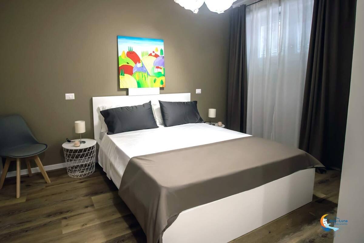 Ein Hotelzimmer mit Bett, Sessel, rundem Tisch, Lampe und einem Bild an der Wand.