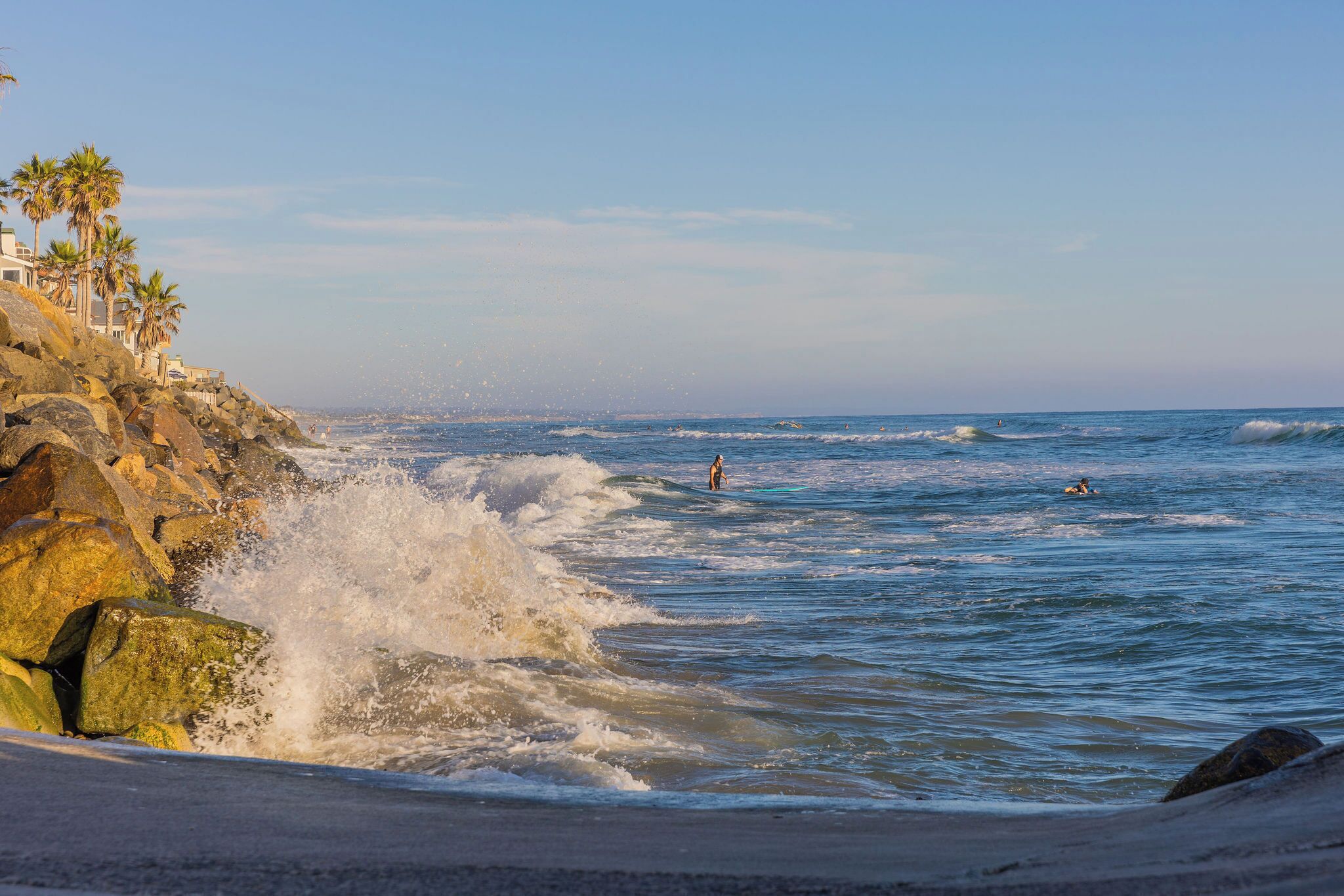 A beach with waves crashing onto rocks and a clear sky.