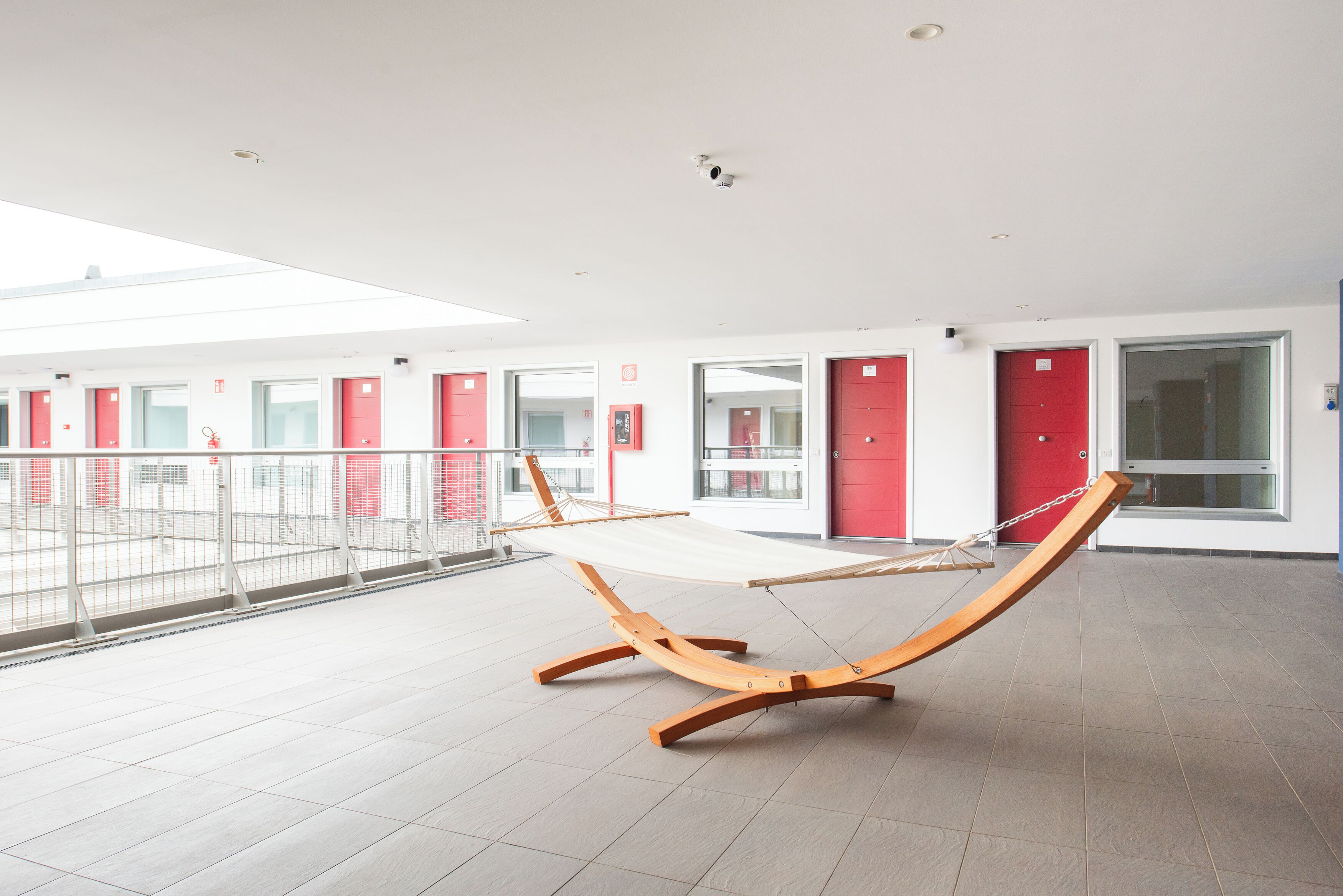 A modern hotel lobby with a hammock, red doors, and a tiled floor.