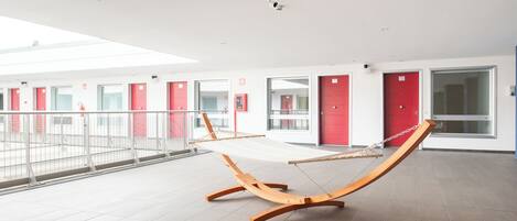 A modern hotel lobby with a hammock, red doors, and a tiled floor.