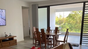 A modern living room with a wooden sofa, a dining table with chairs, a TV mounted on the wall, and a large window with a view of greenery. - Impeccable Luxury 3-bed Apartment in Albion (Albion)