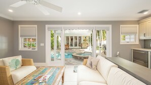 A modern living room with a sofa, coffee table, and a view of a swimming pool and outdoor area.