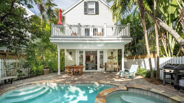 A backyard with a swimming pool, a deck with outdoor furniture, and a house with a balcony.
