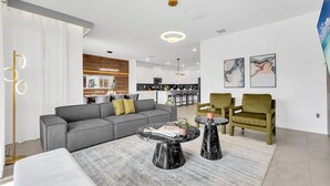 Un salon moderne avec un canapé gris, deux petites tables rondes noires et des fauteuils verts.
