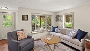 A living room with a gray sofa, a beige sofa, a wooden coffee table, and a window seat with a view of greenery. - Cozy riverfront cabin on the New River.  Close to Boone and Appalachian State. (Boone)