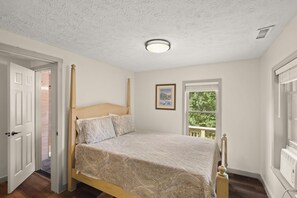 Un dormitorio con cama con dosel, una lámpara de techo, un ventanal con vistas y una puerta que da a otra habitación.