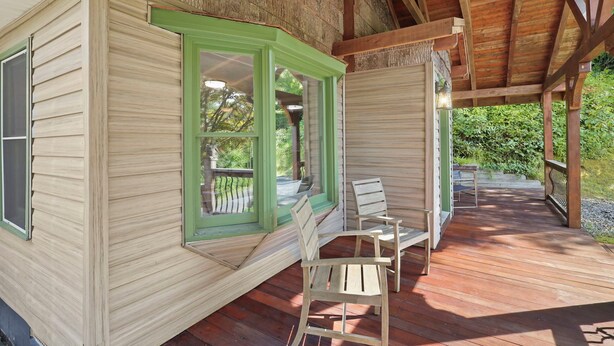 A wooden cabin with a green-framed window, a wooden deck, and two wooden chairs. - Cozy riverfront cabin on the New River.  Close to Boone and Appalachian State. (Boone)