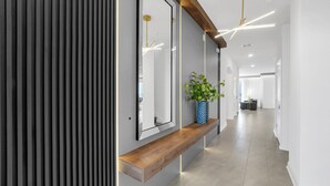 Um corredor moderno com um banco de madeira, um espelho grande e um vaso com planta.