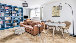 A living room with a blue bookshelf, a brown sofa, a round dining table with chairs, and a map on the wall. - Stylish Flat Close To Beach - Pass the Keys (Chichester)