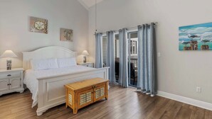 Une chambre à coucher comprenant un lit, des tables de chevet, un banc en bois, un ventilateur de plafond et une vue sur un balcon avec des rideaux.