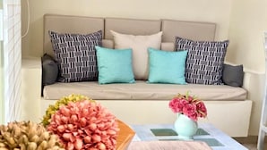 A living room with a beige sofa, patterned cushions, a wooden coffee table, and a vase with flowers. - SM Apartments (San José del Cabo)