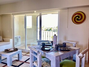 A dining area with a table set for two, a chair, and a small table with a basket. - SM Apartments (San José del Cabo)