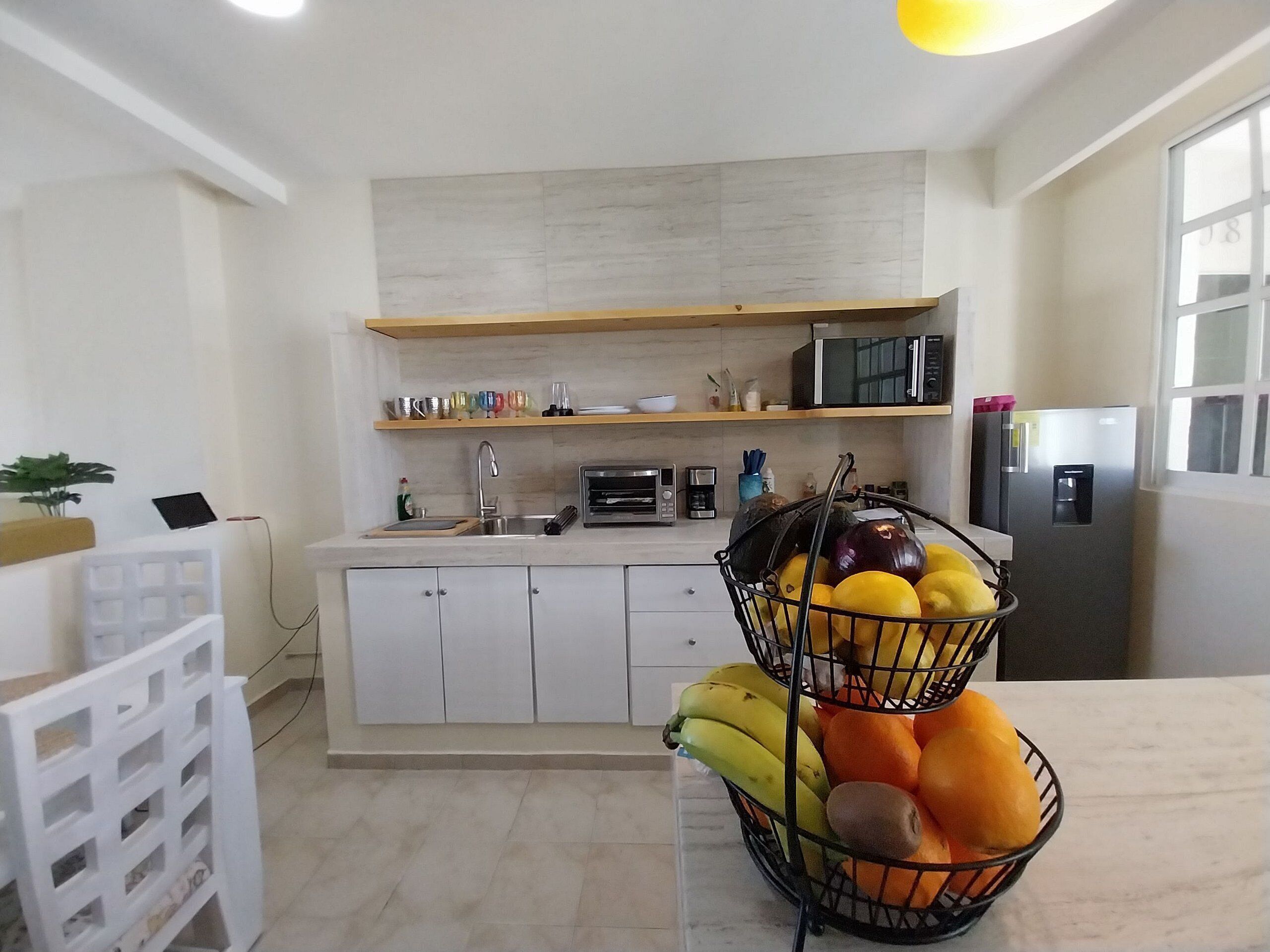 Una cocina moderna con armarios blancos, un microondas, un refrigerador y una cesta de fruta sobre la encimera.