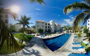 A swimming pool area with lounge chairs, palm trees, and modern buildings. - SM Apartments (San José del Cabo)
