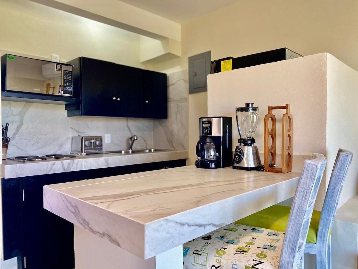 Een moderne keuken met een marmeren aanrecht, zwarte kastjes, een magnetron, een broodrooster, een koffiezetapparaat en een blender.