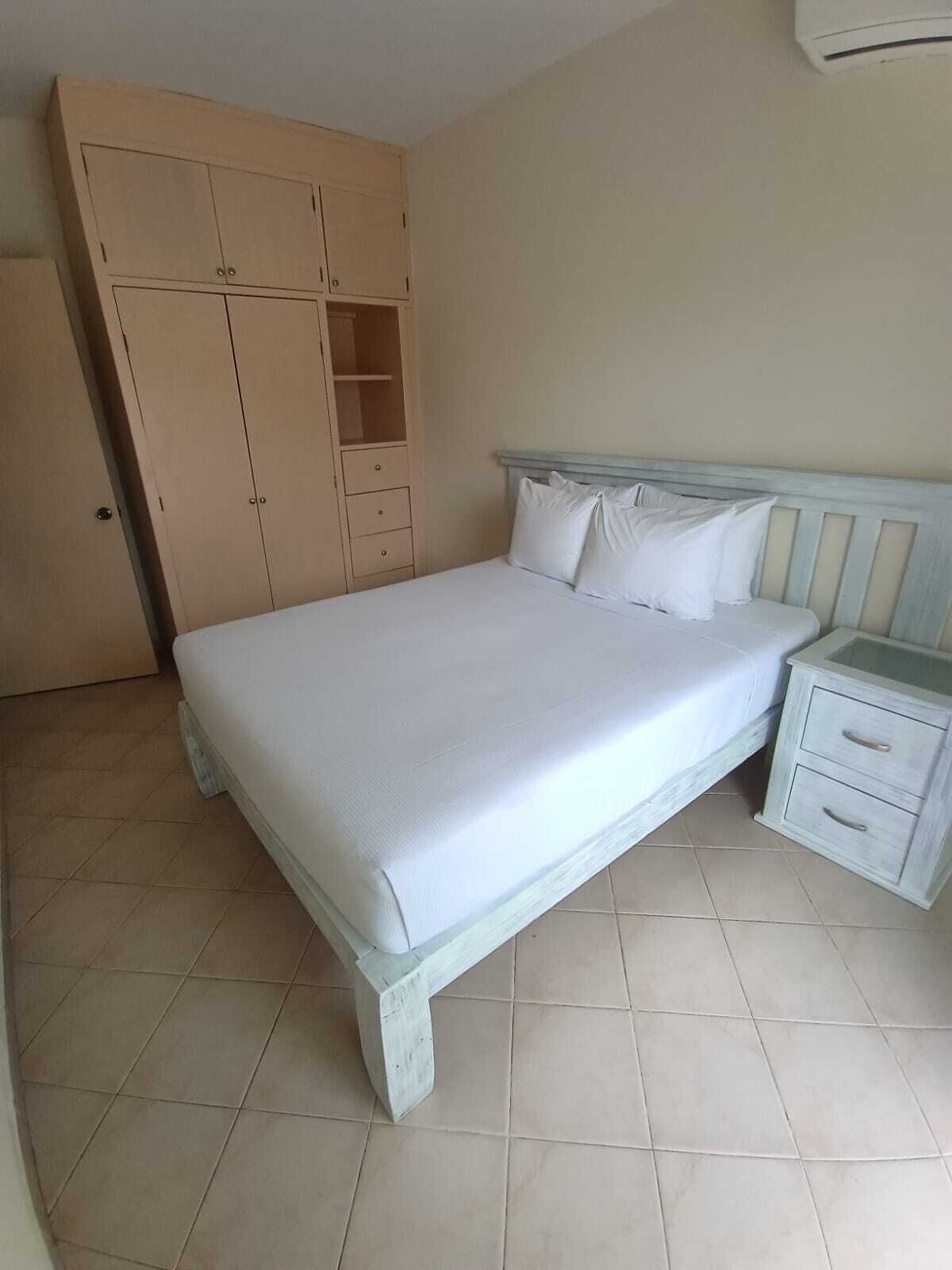 Een slaapkamer met een bed, nachtkastje, kledingkast en betegelde vloer.