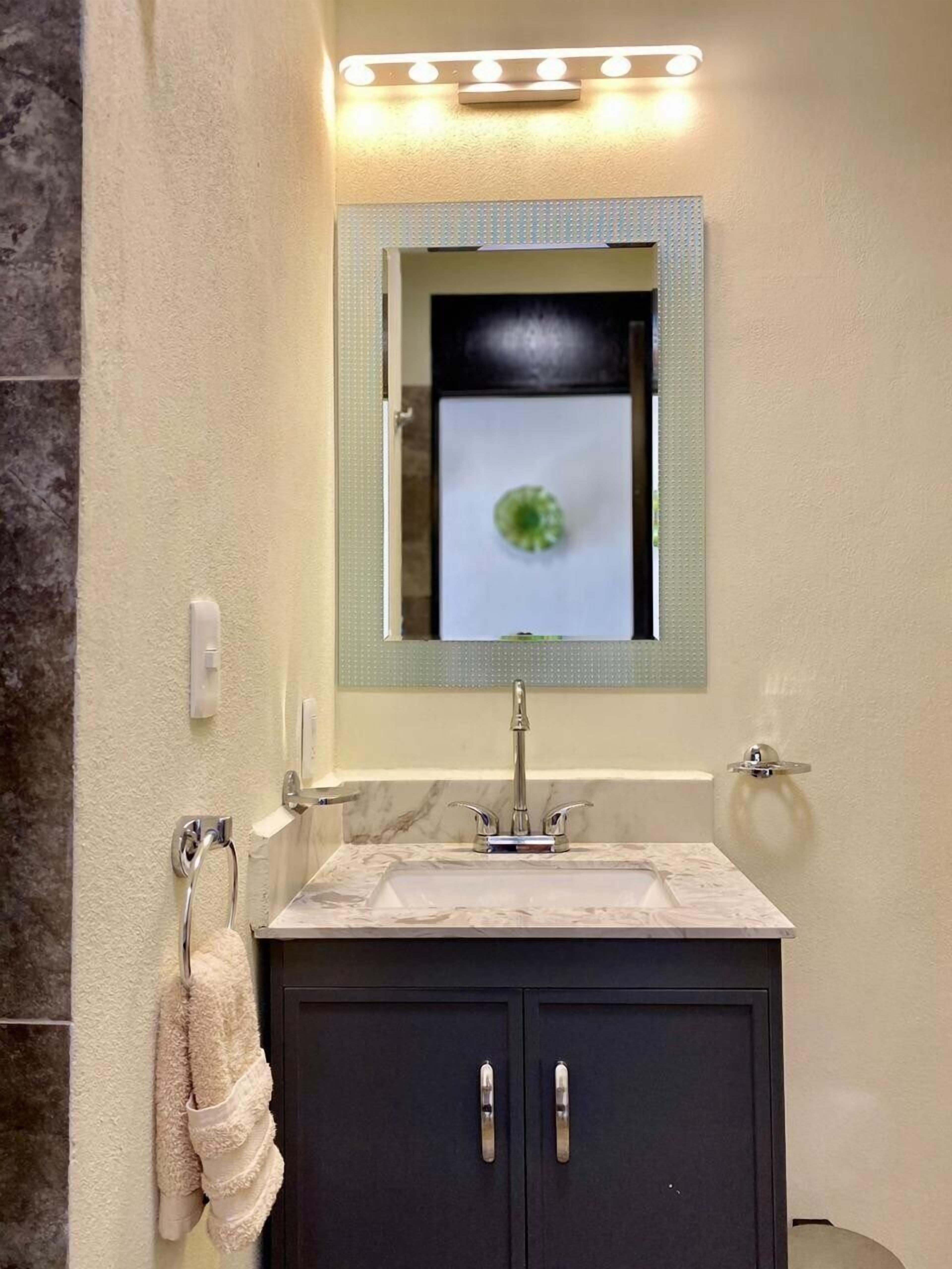 Une salle de bain avec un lavabo en marbre, un meuble sombre, un porte-serviettes et un miroir avec des lumières au-dessus.
